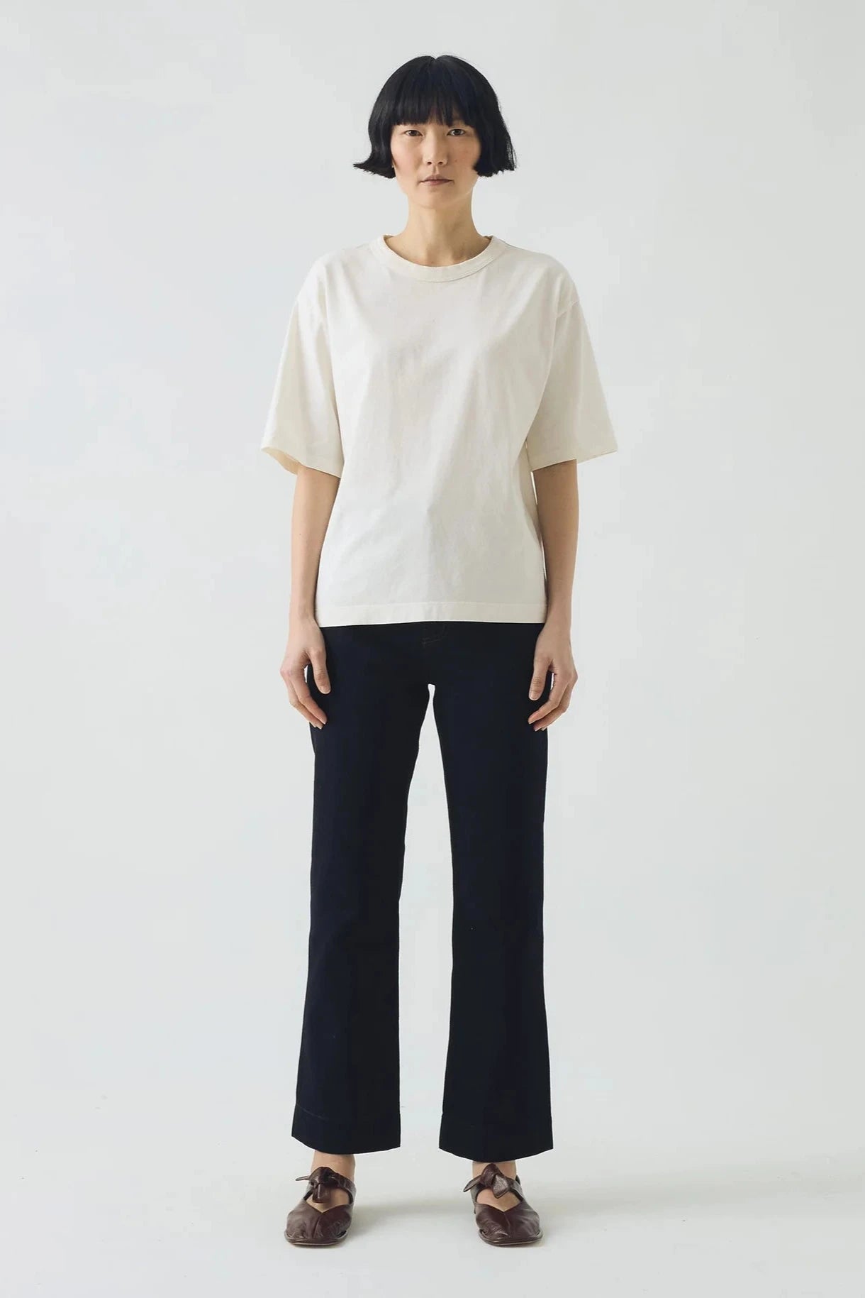 Person wearing a white shirt and black pants on a plain background
