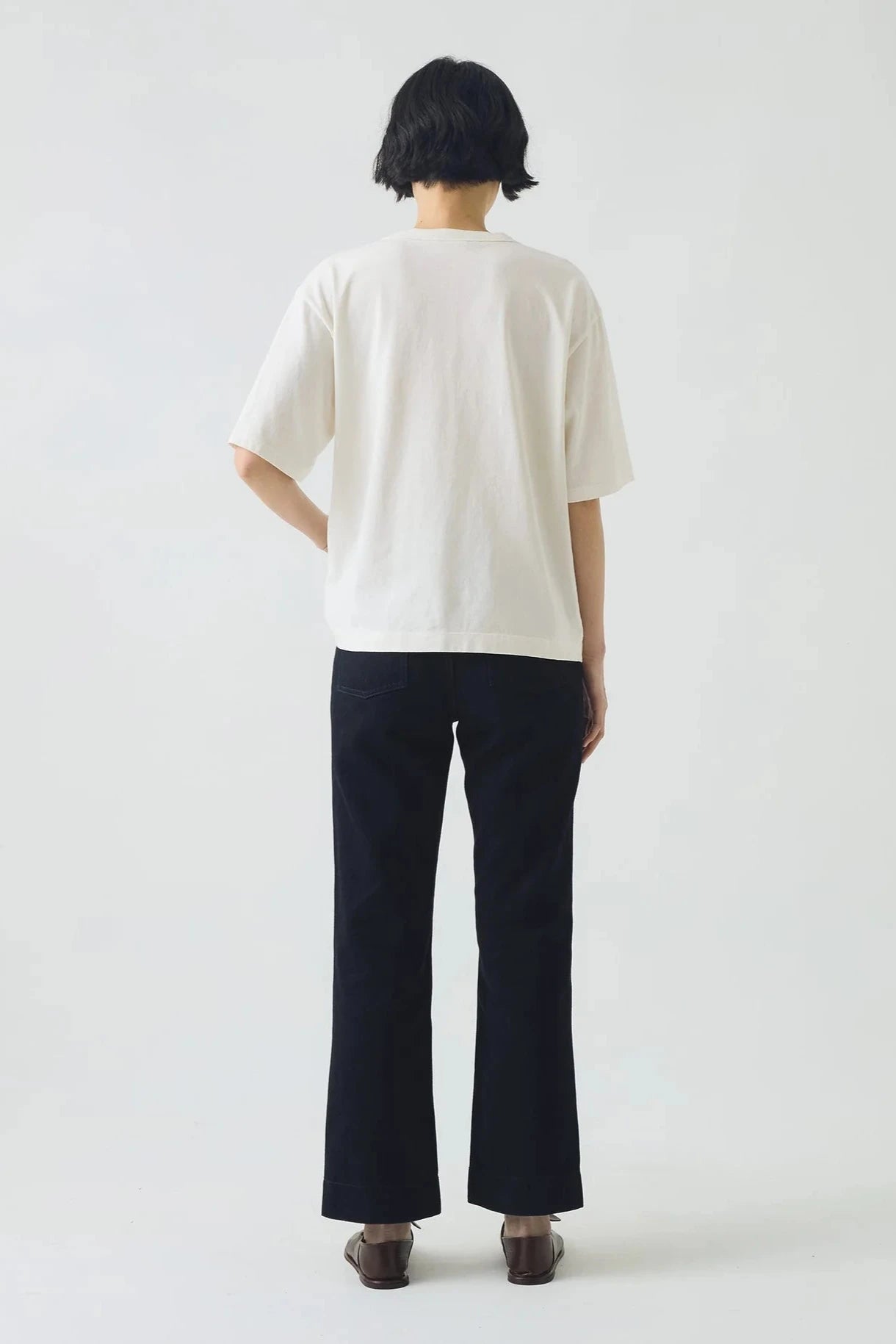 Person wearing a white shirt and dark pants on a plain background, viewed from the back
