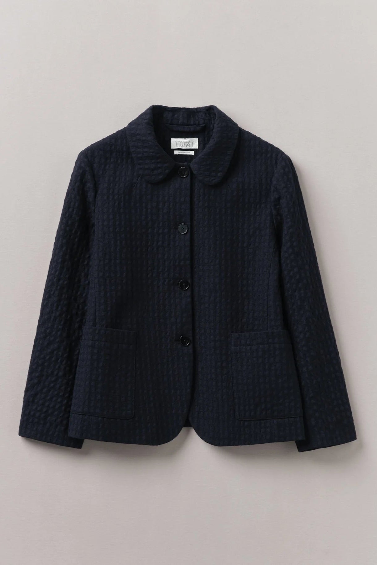 A navy blue cotton wool herringbone jacket with a collar, buttons, and a tailored fit on a plain background.