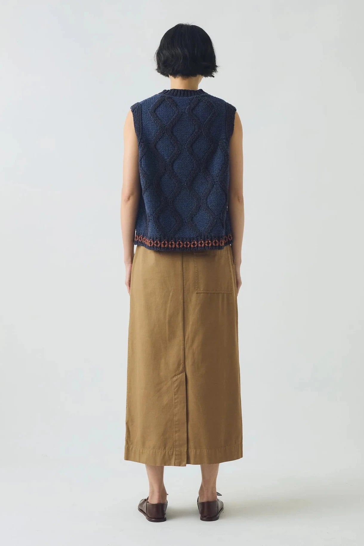 Person wearing a navy patterned vest over a beige dress on a white background, viewed from the back