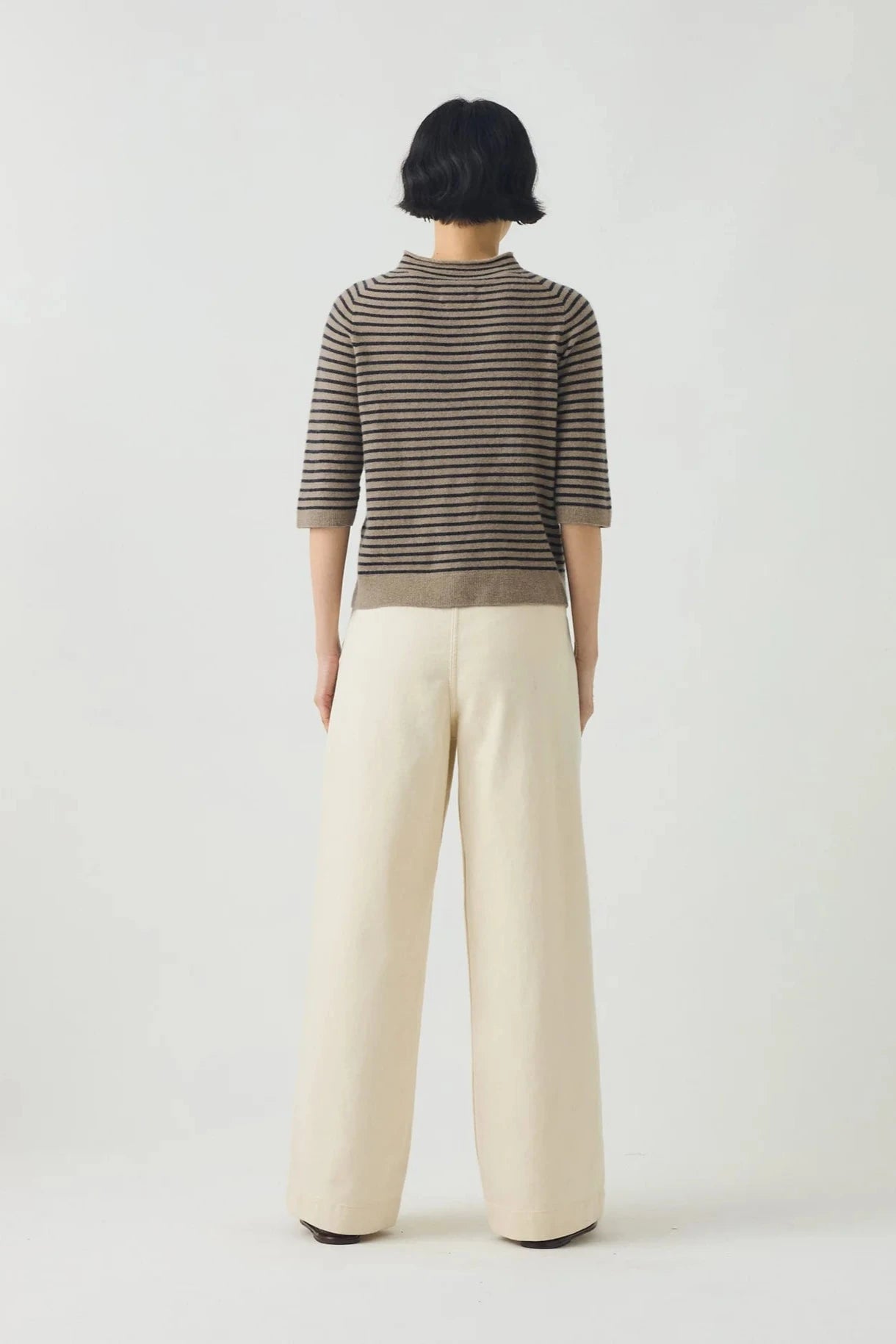 Person wearing a striped sweater and beige pants on a white background, viewed from the back