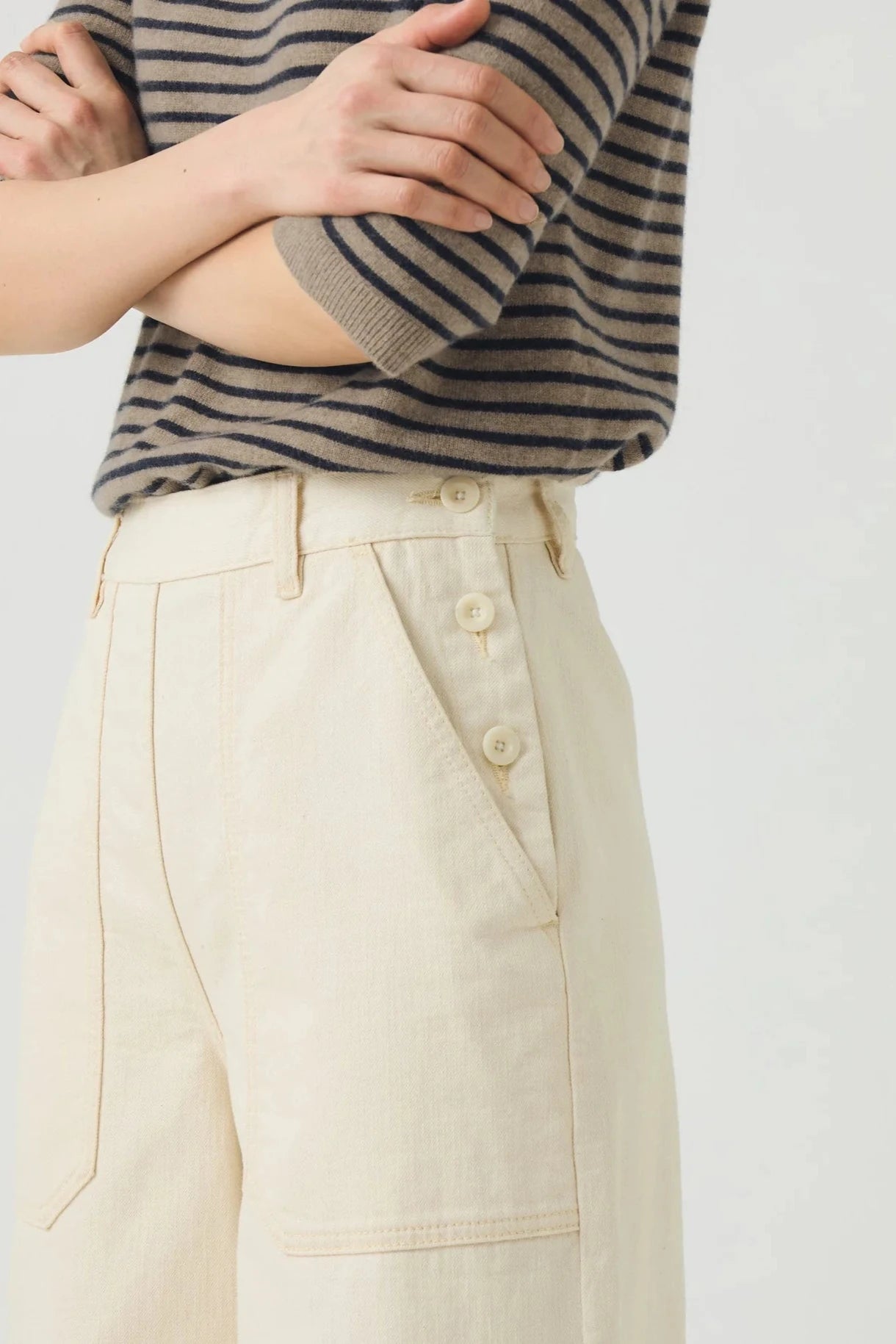 Person wearing a striped sweater and beige pants on a plain background, close p vew of pockets and button details.