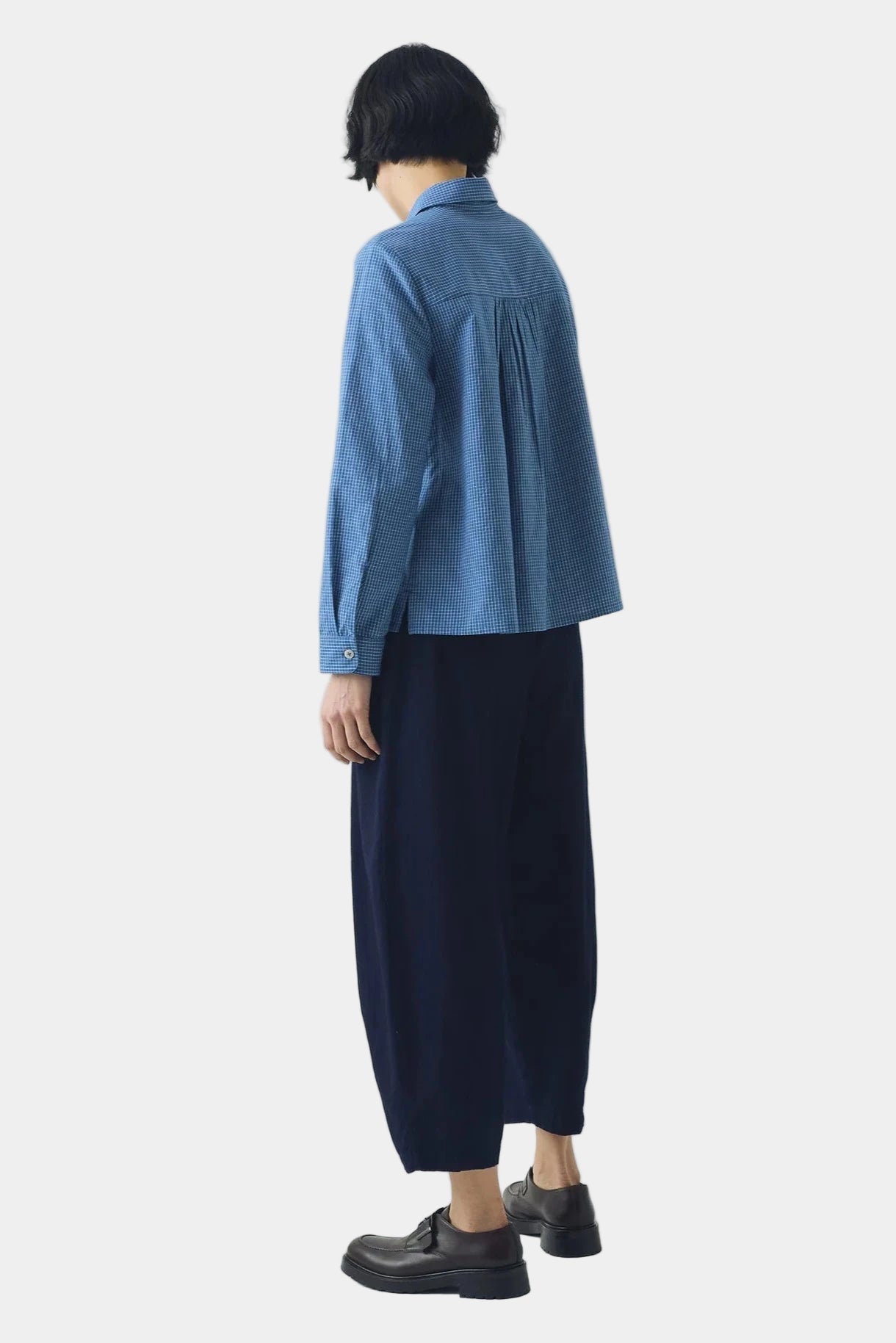 Person wearing a blue shirt and dark pants on a white background, viewed from the back