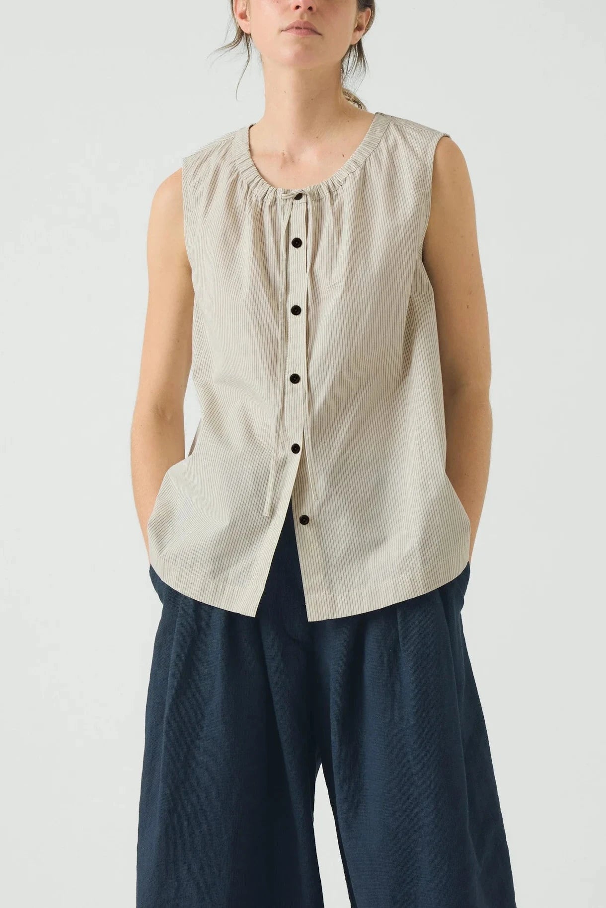 Beige sleeveless blouse with buttons on a light gray background