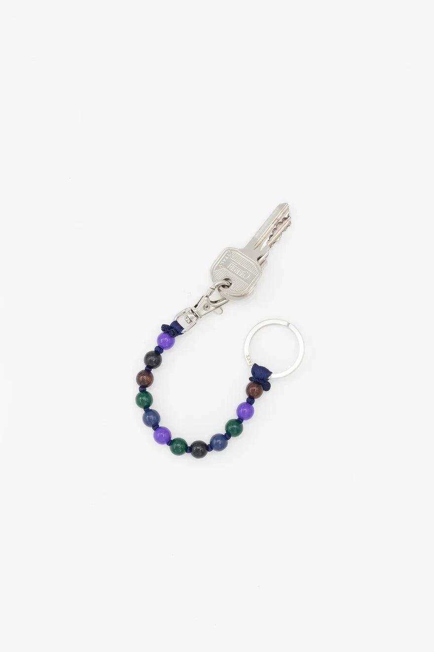 A keychain with a purple and dark green beaded chain and silver metal components on a white background.