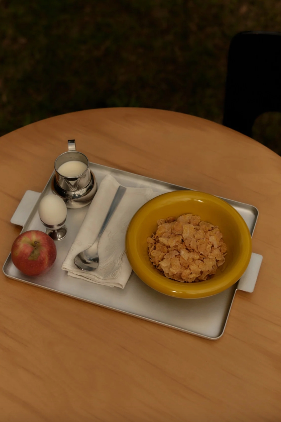 Yellow bowl of cereal on a tray with an apple and milk container on a wooden table.