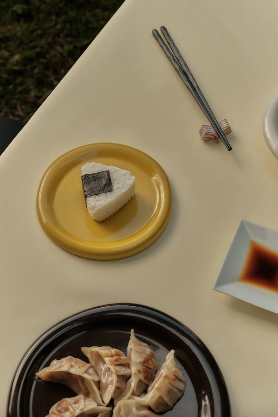 sushi on a yellow plate, surrounded by other food items on a beige table.