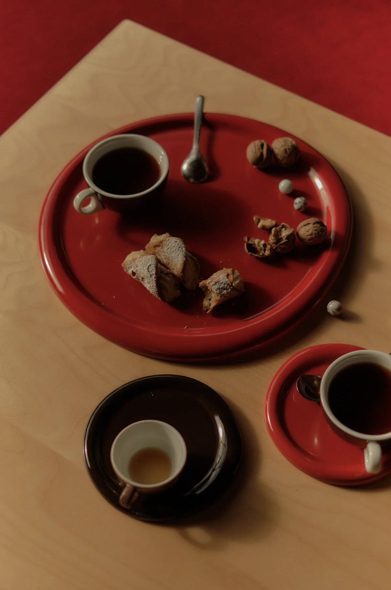 Three coffee cups on red and black plates with cookies and a spoon on a wooden surface.