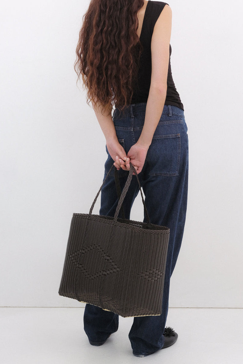 Person holding a woven handbag against a white background