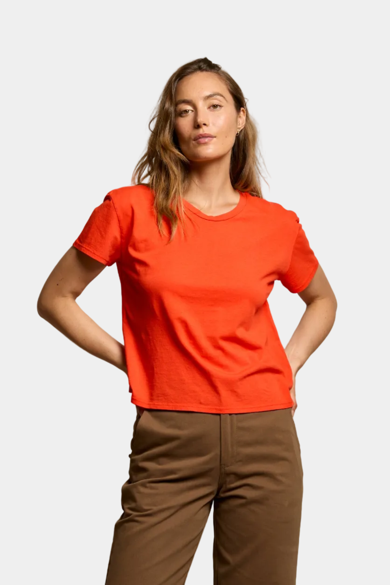 Woman wearing a bright red t-shirt and brown pants on a white background