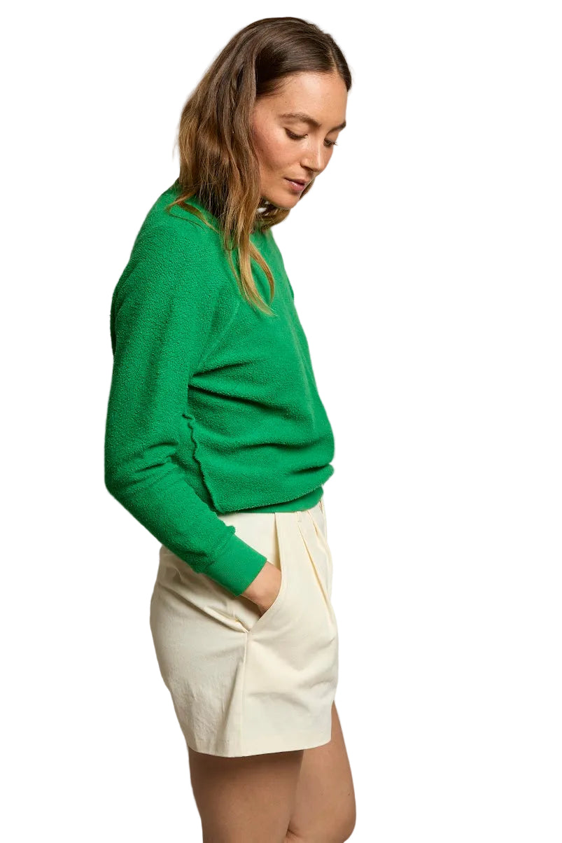 Woman wearing a green sweater and white shorts against a plain background