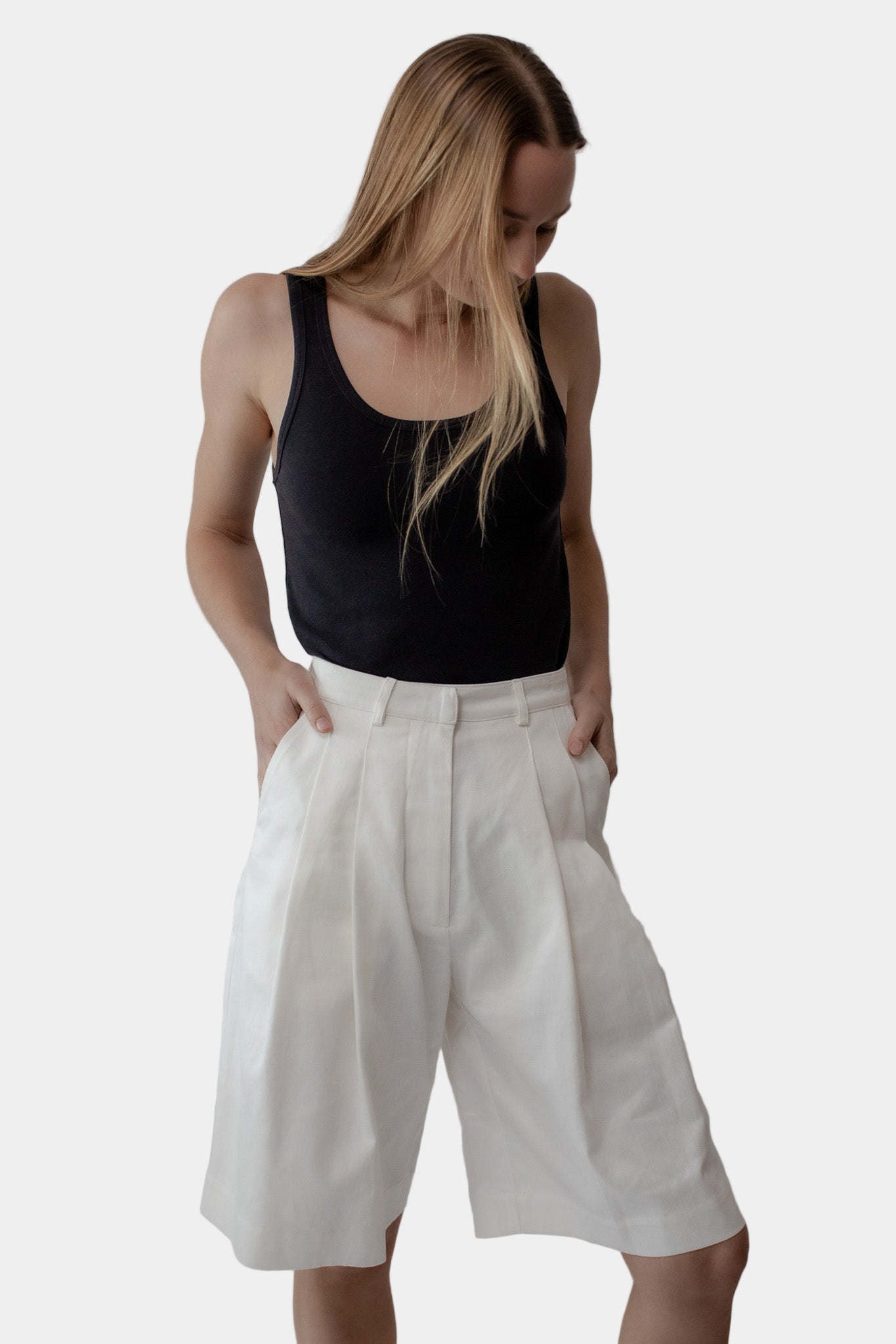 A person wearing a black tank top and white tailored shorts with a double front pleat and side entry pockets.