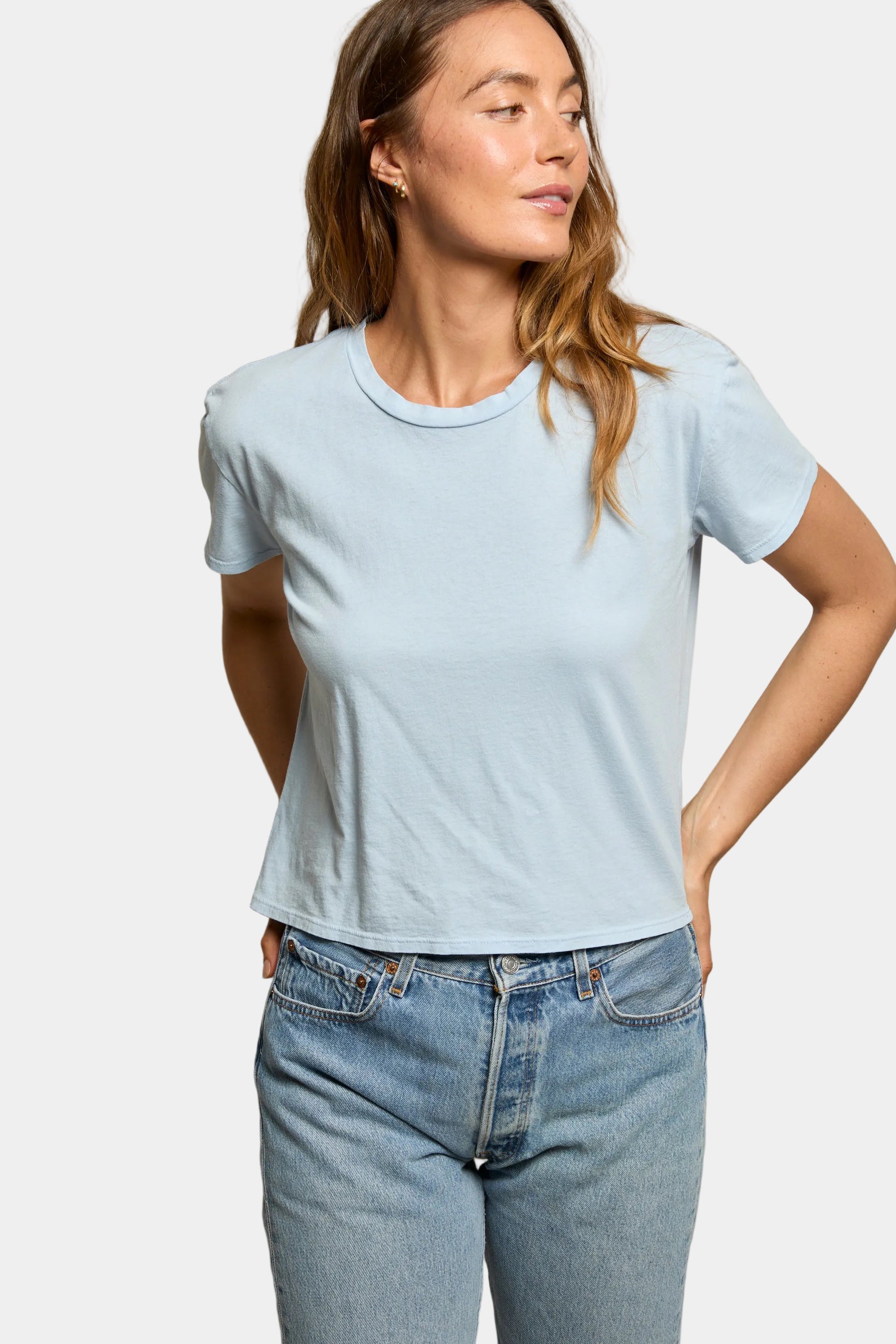 Woman wearing a light blue t-shirt and jeans against a beige background
