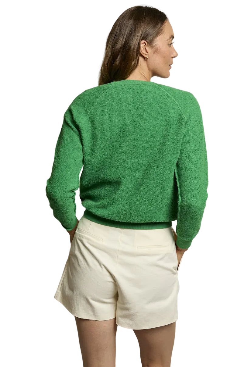 Woman wearing a green sweater and beige shorts against a neutral background