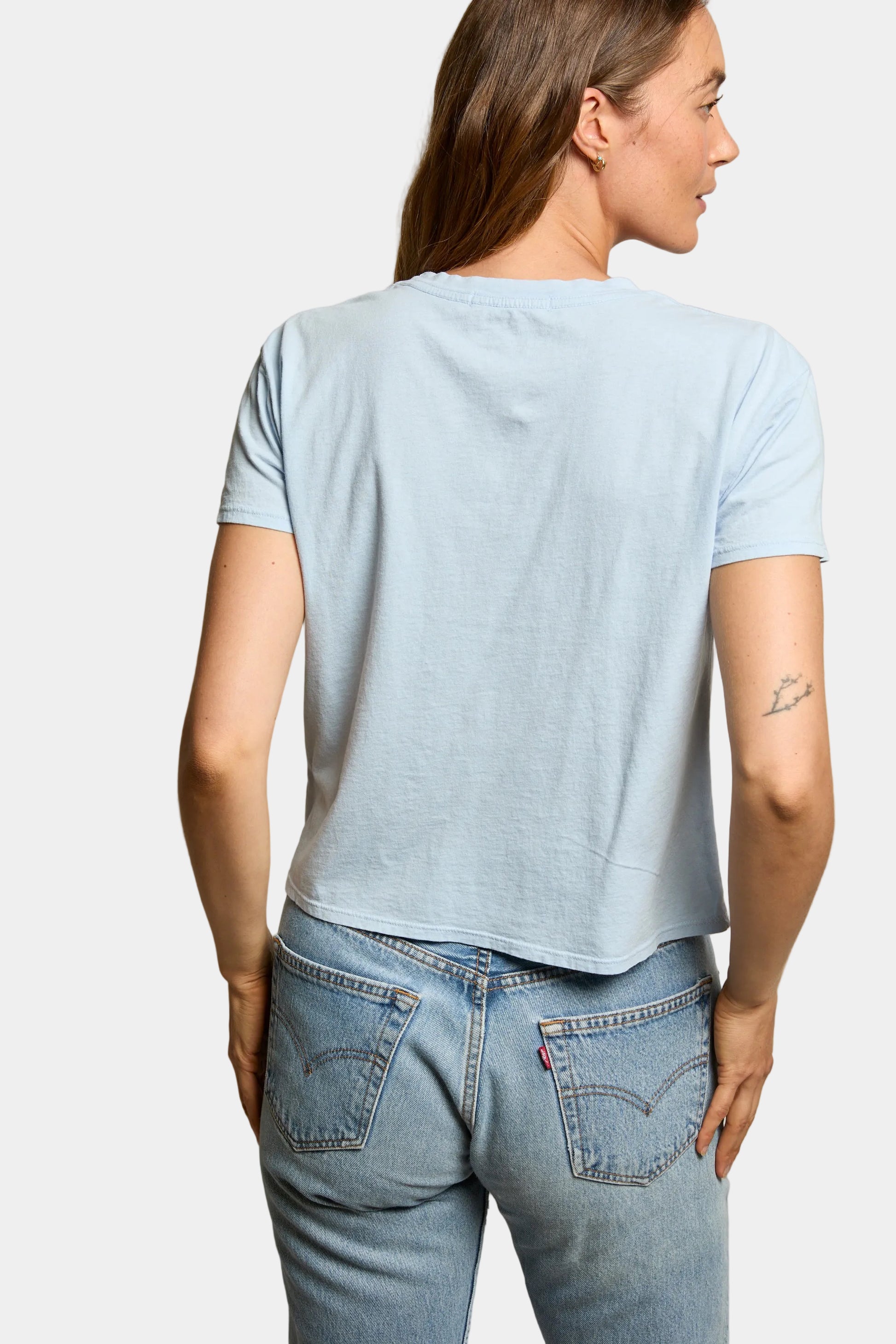 Woman wearing a light blue t-shirt and jeans against a plain background