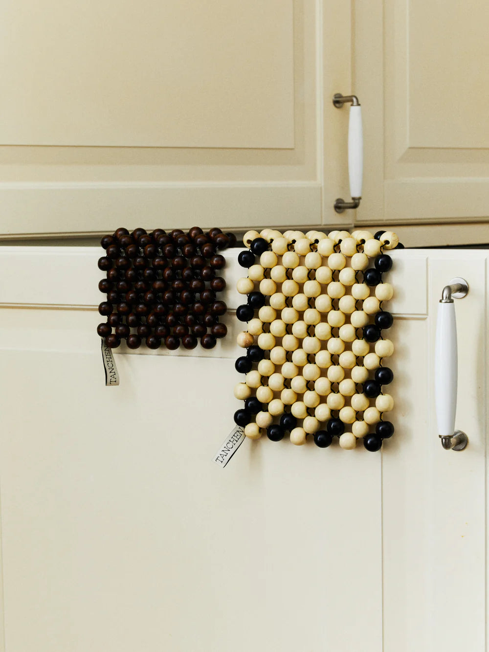 Two decorative wall hangings with black and white bead patterns on a kitchen cabinet.
