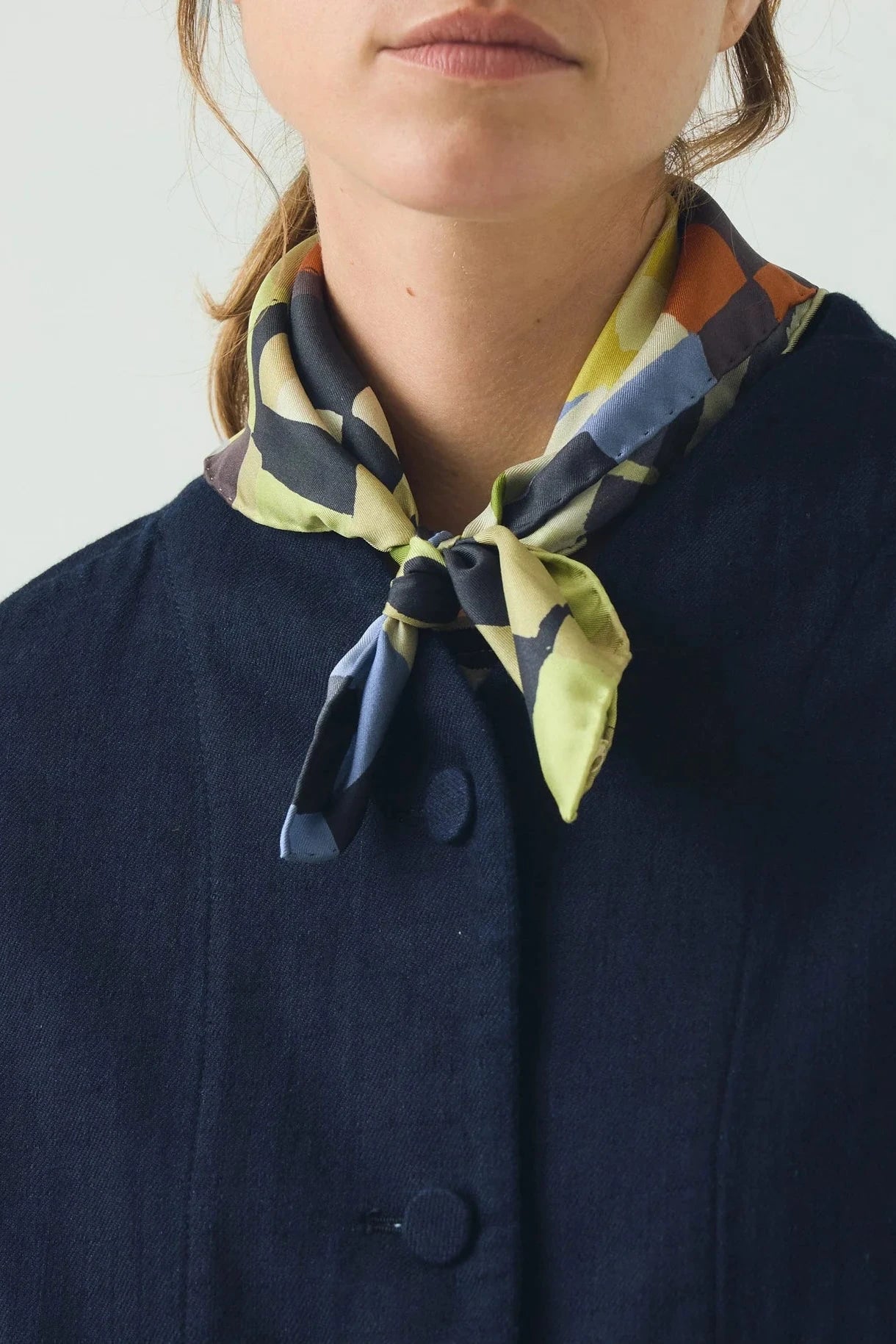 Person wearing a colorful scarf around their neck with a plain background