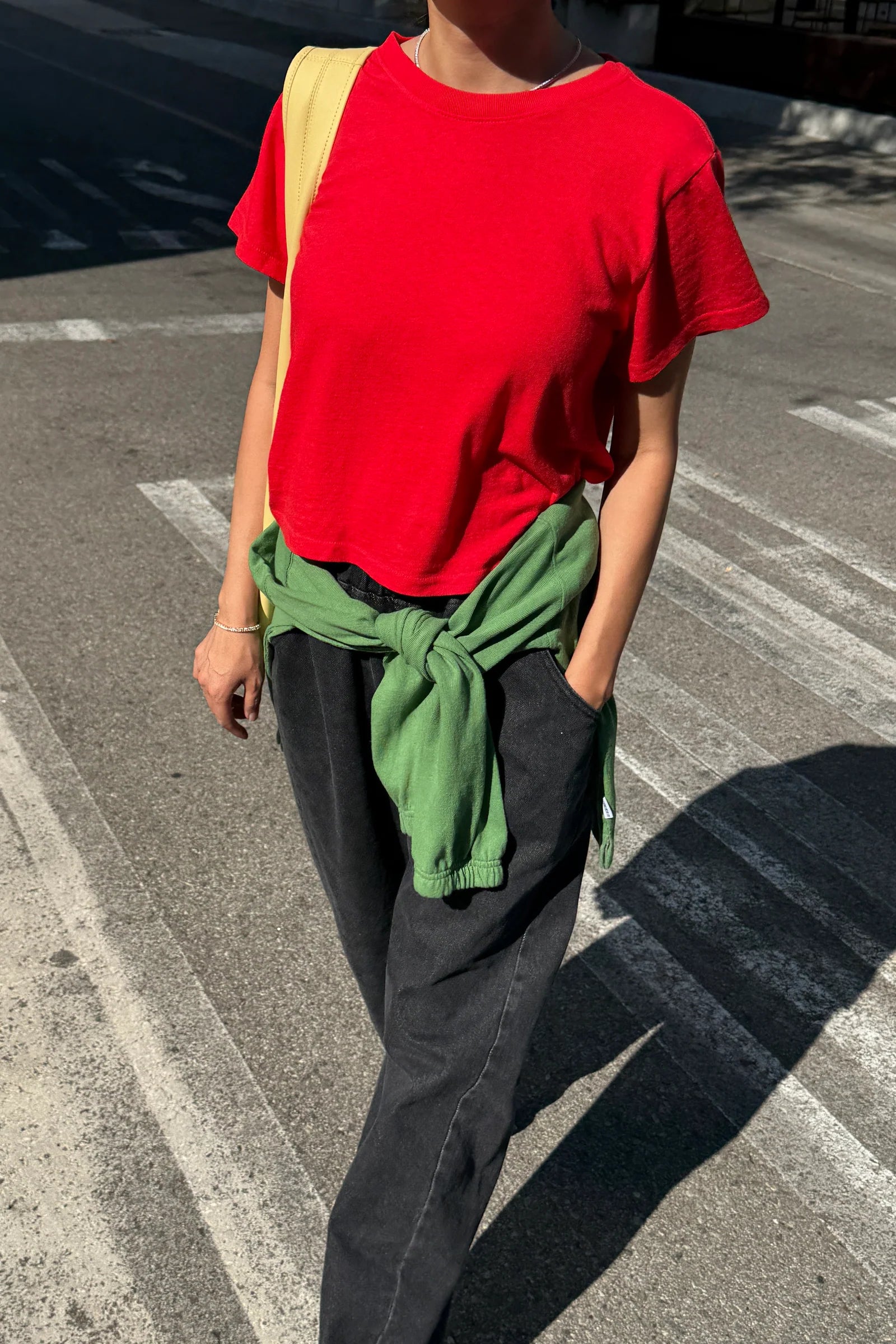 A person wearing the Le Bon Shoppe Airy Tee in tomato, styled with black wide leg jeans and a green sweater around the waist- East Coast General