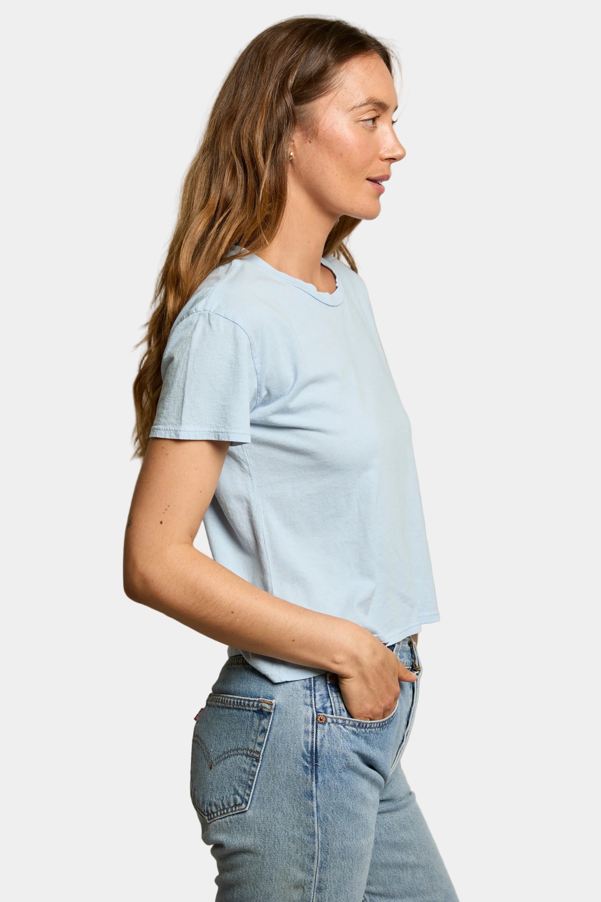 Woman wearing a light blue t-shirt and jeans against a soft grey background