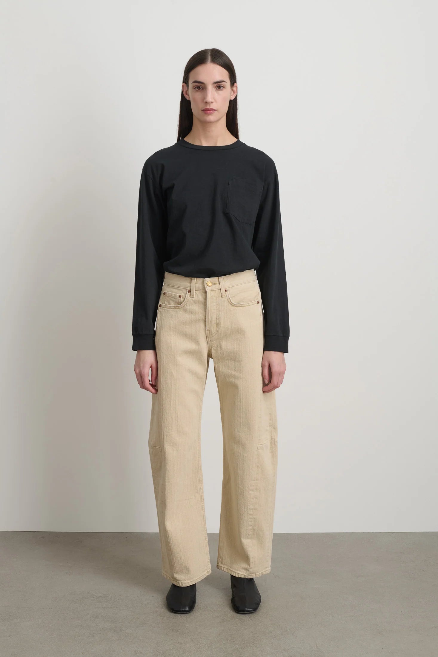 Person wearing a black sweater and beige pants against a plain background
