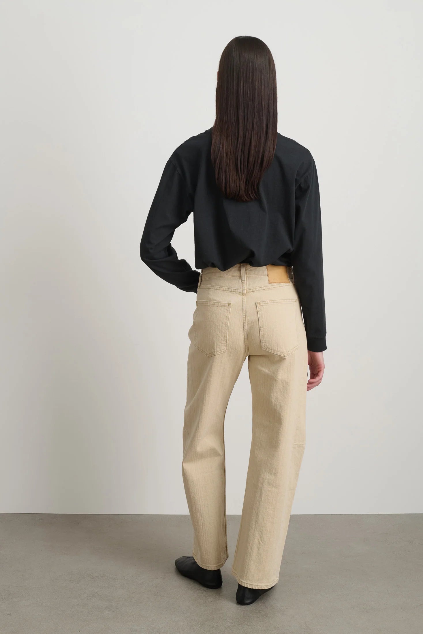 Person wearing a black shirt and beige pants against a plain background