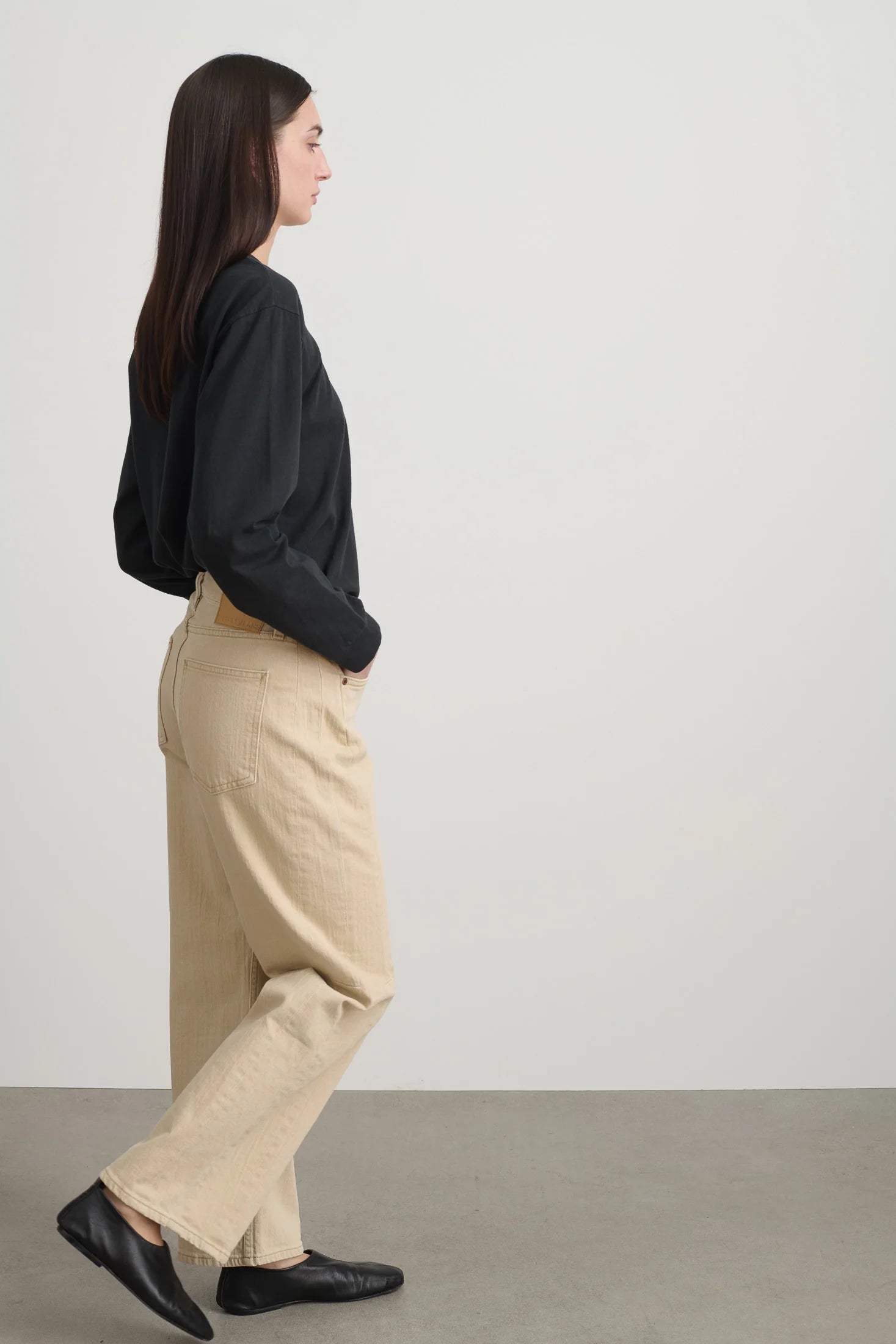 Person wearing a black shirt and beige pants standing against a white background