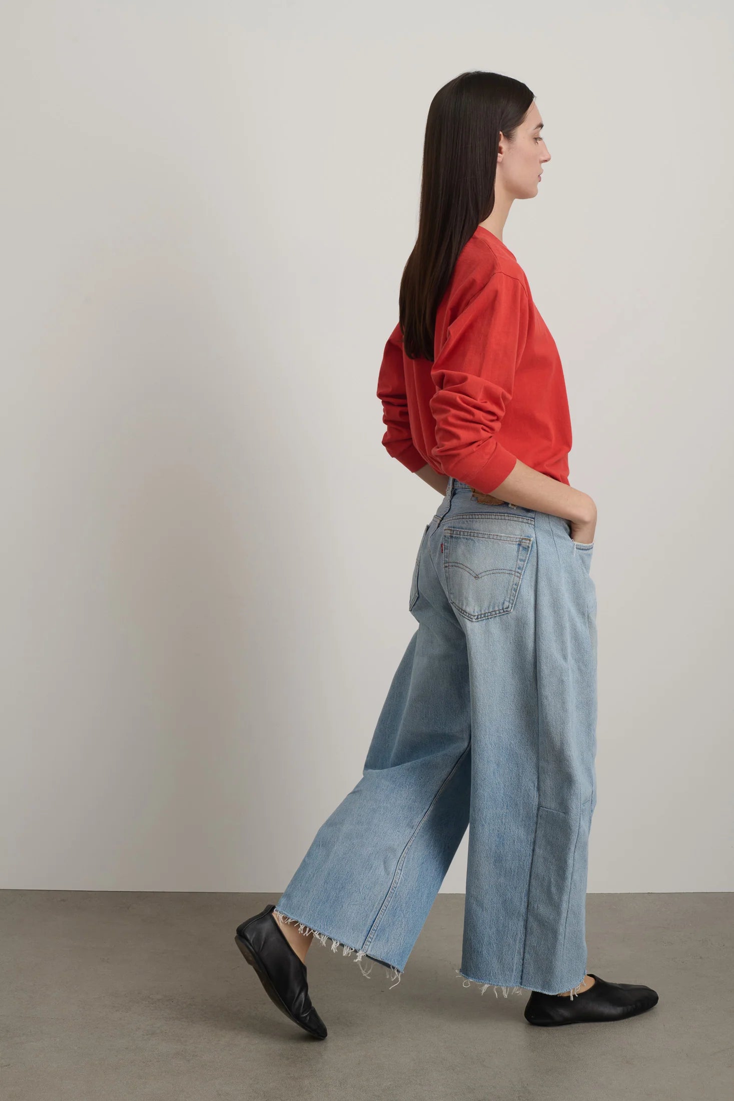 Woman wearing a red sweater and light blue jeans against a plain background