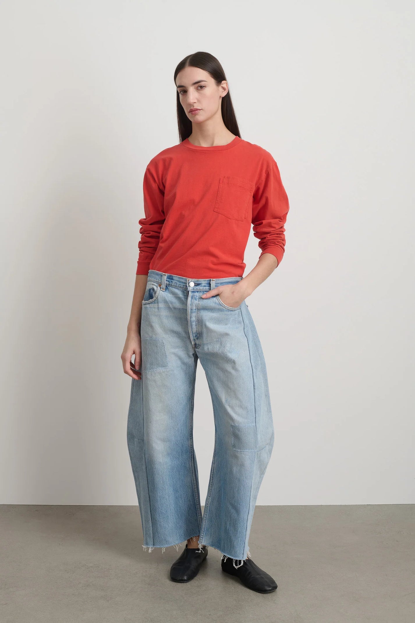 Person wearing a red sweater and light blue jeans against a plain background