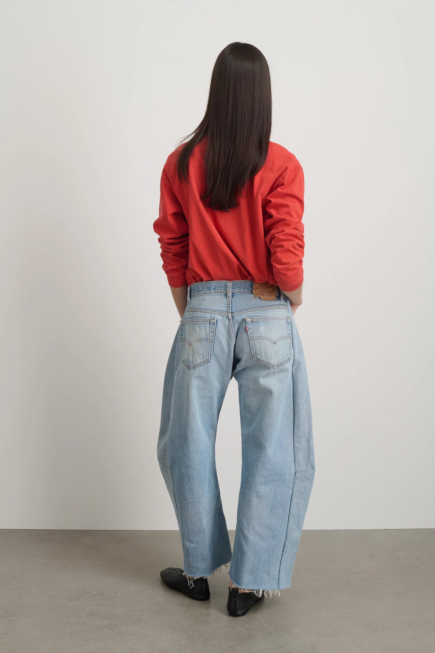 Person wearing a red sweatshirt and light blue jeans standing against a plain white wall.