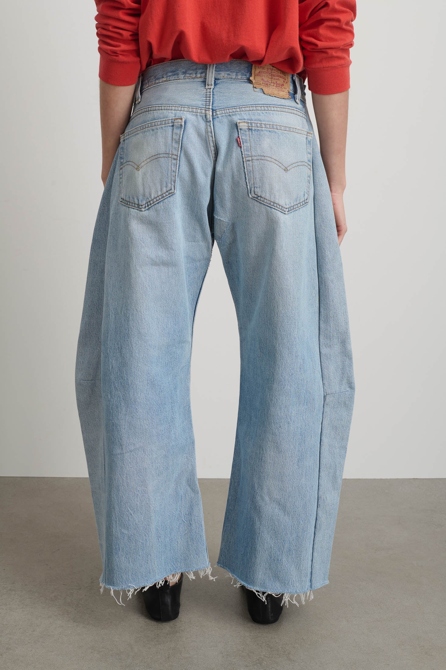 Person wearing light blue jeans with a red top on a plain background