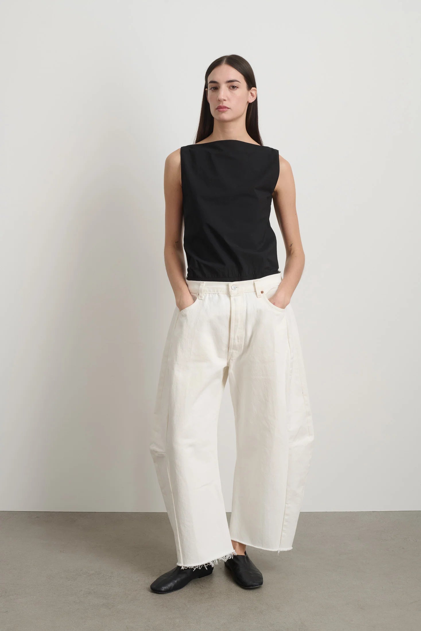 Woman wearing a black sleeveless top and white wide-leg pants against a plain background