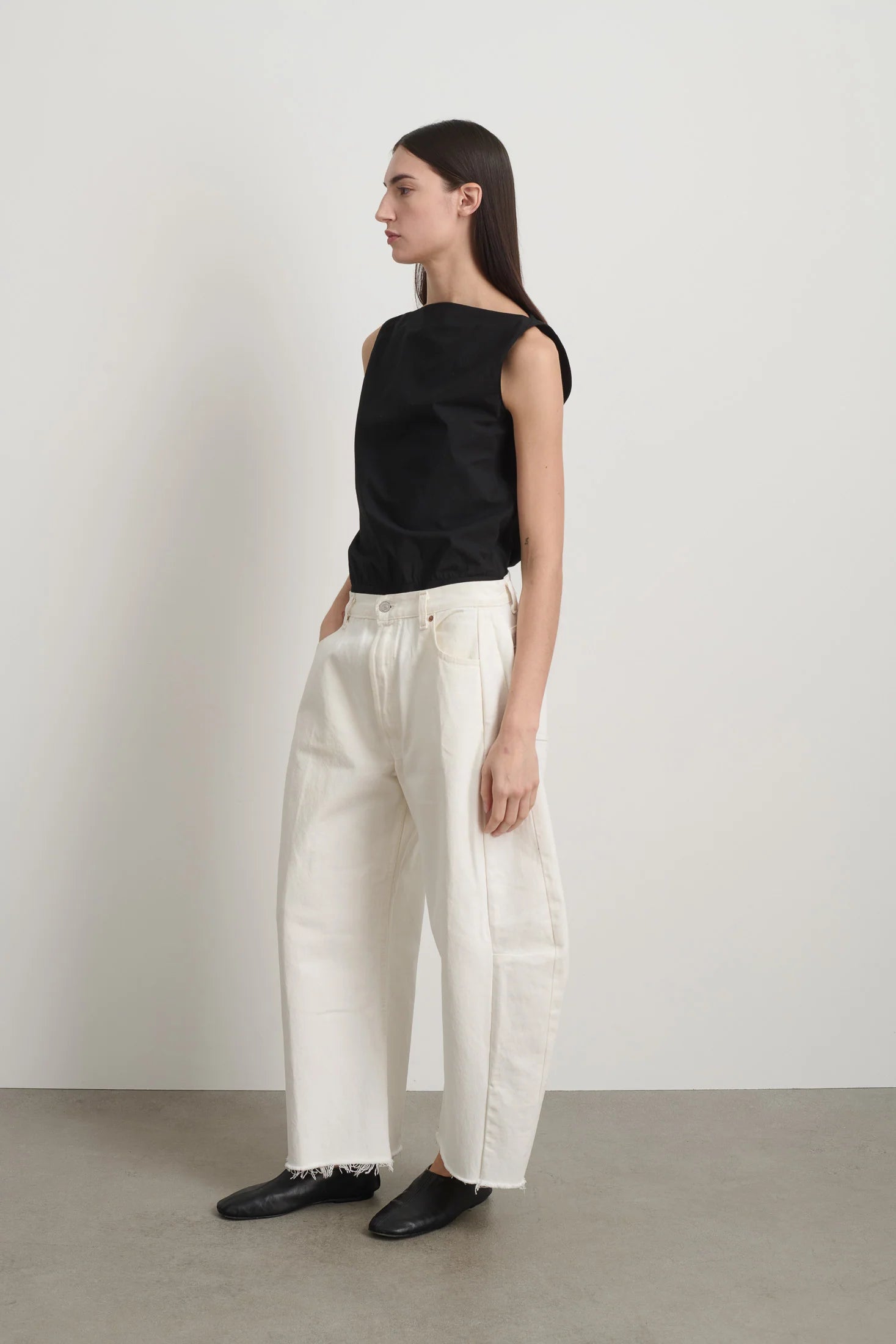 Person wearing a black sleeveless top and white pants against a plain background