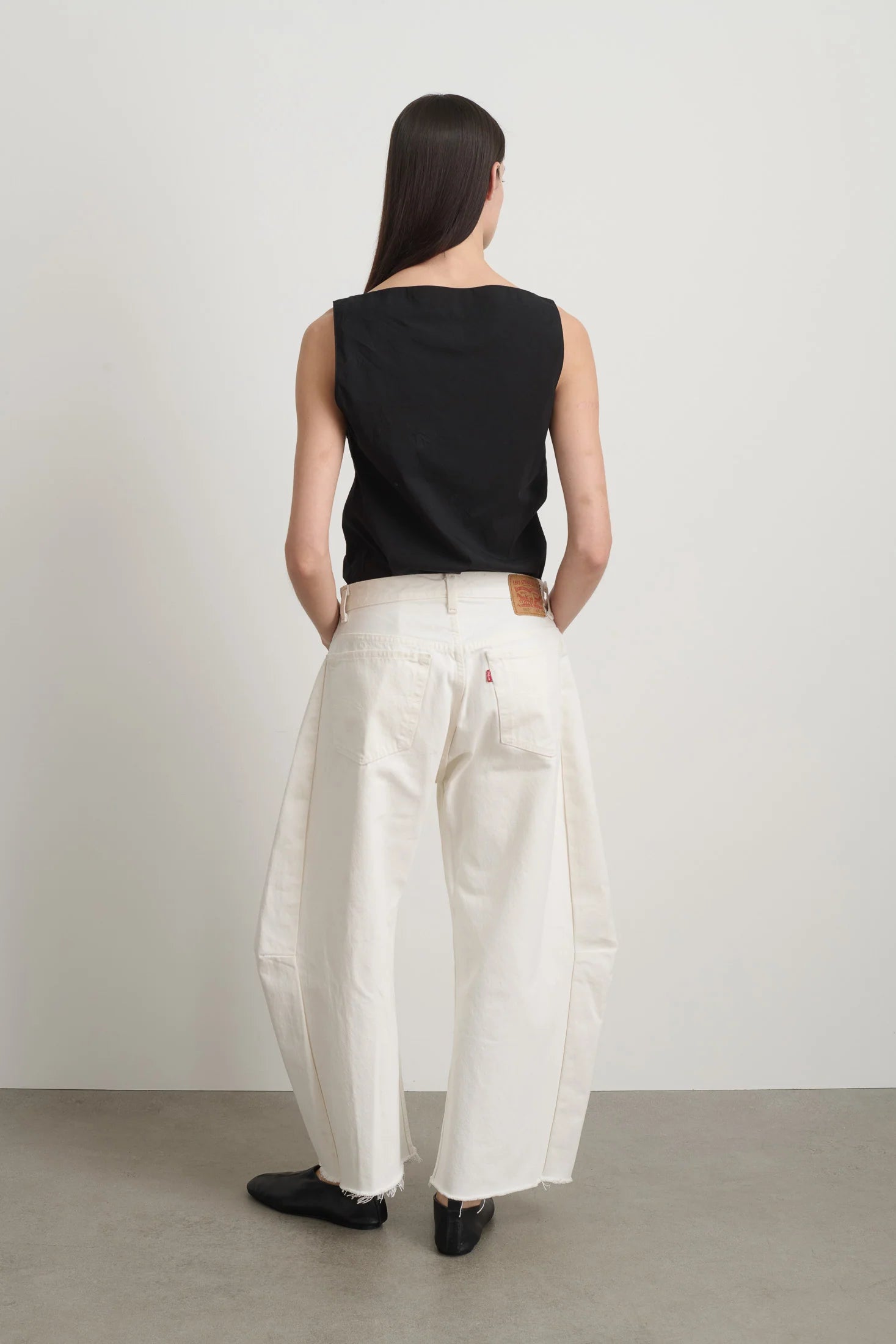 Person wearing a black sleeveless top and white pants standing against a plain background