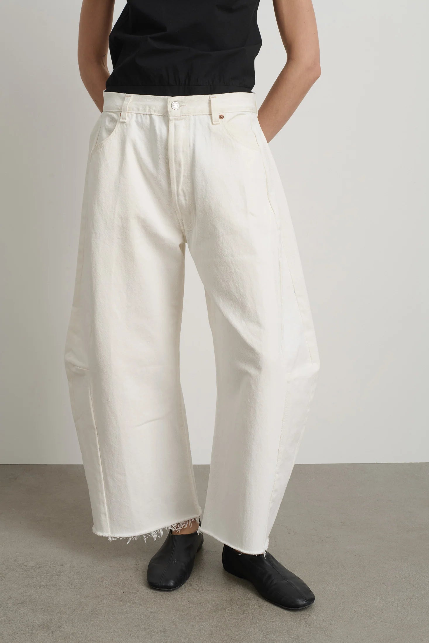 Person wearing white wide-leg pants and black shoes on a plain background