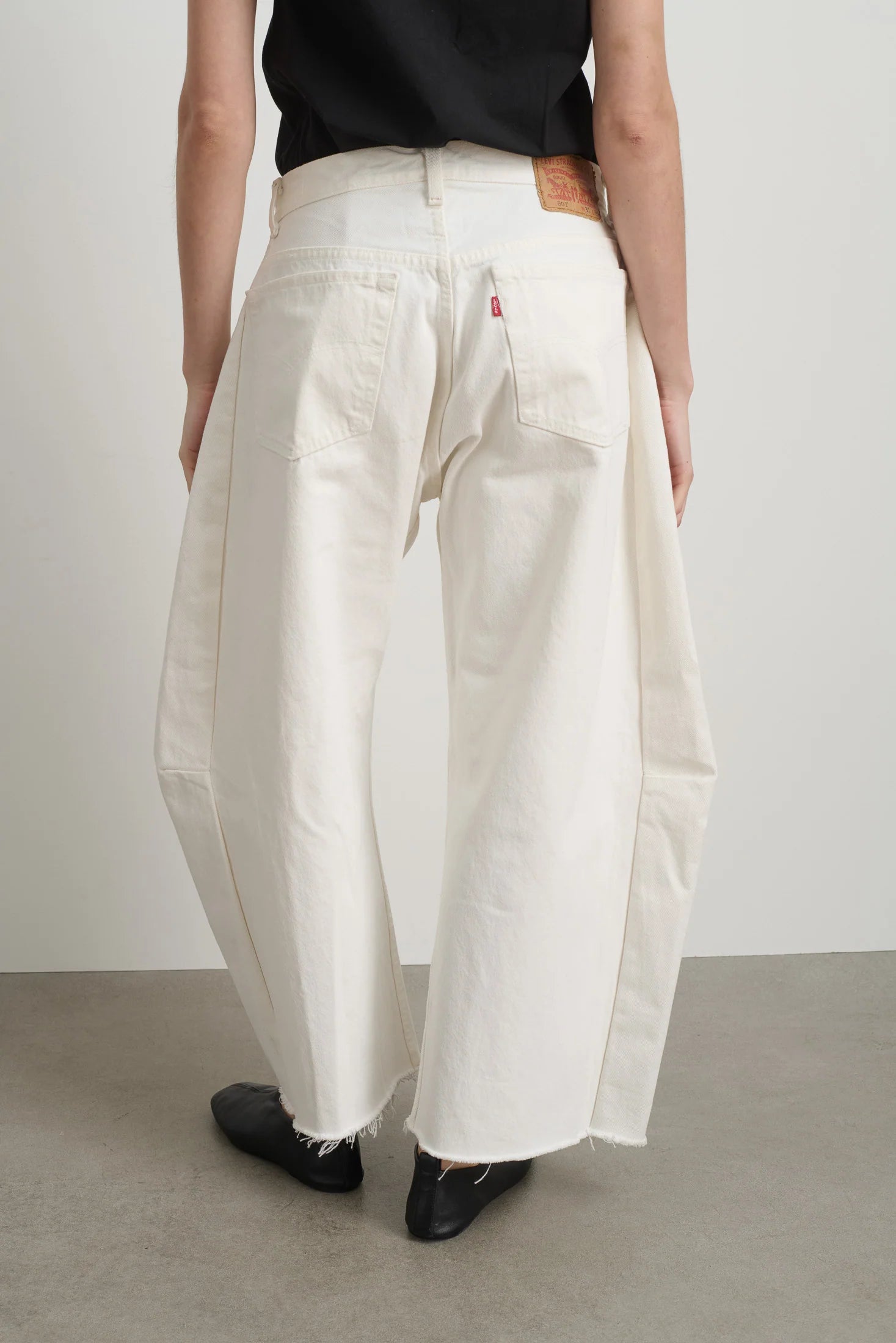 Person wearing white wide-leg pants and black shoes on a plain background