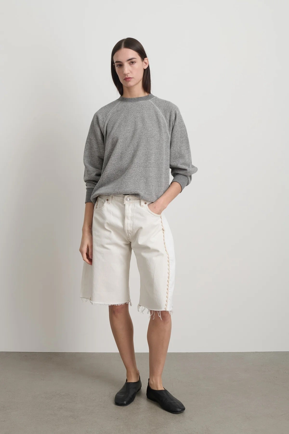 Person wearing a gray sweater and white shorts against a plain background