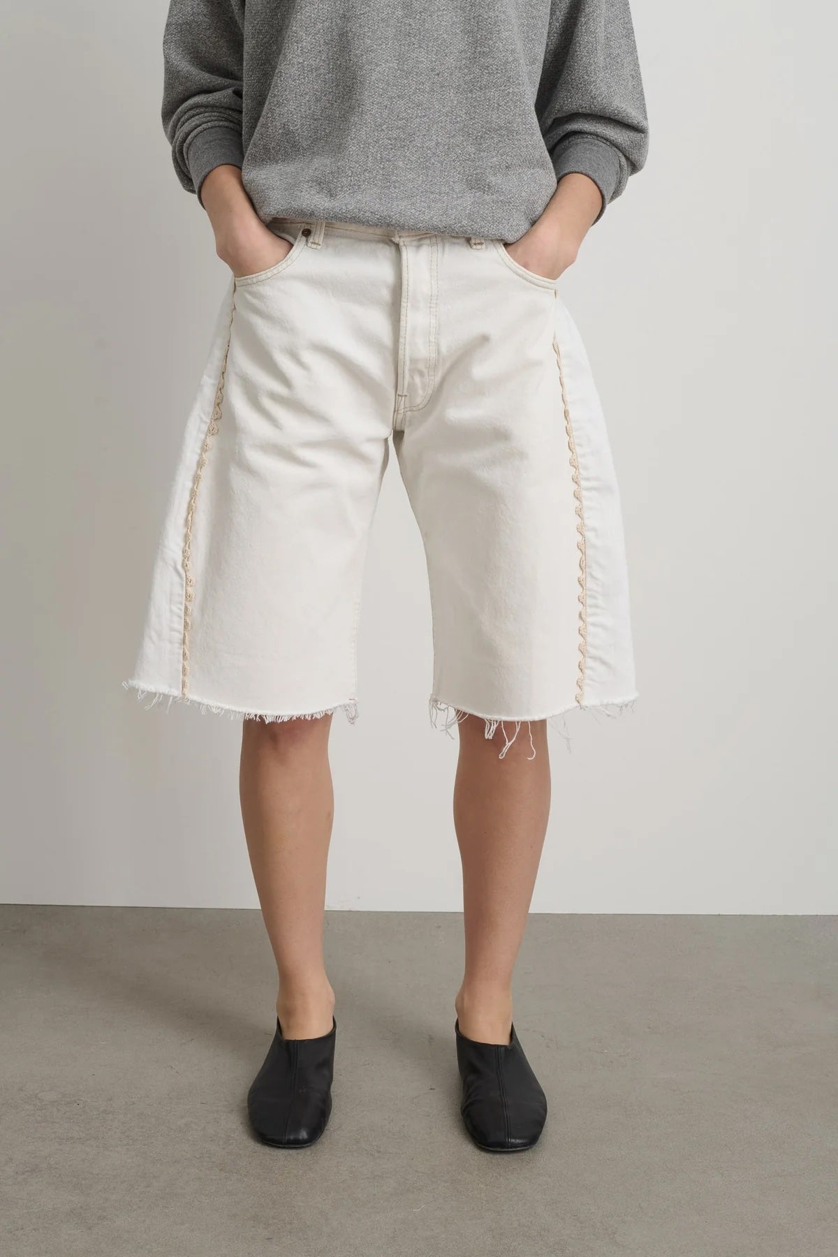 Person wearing a gray sweater and white shorts against a plain background