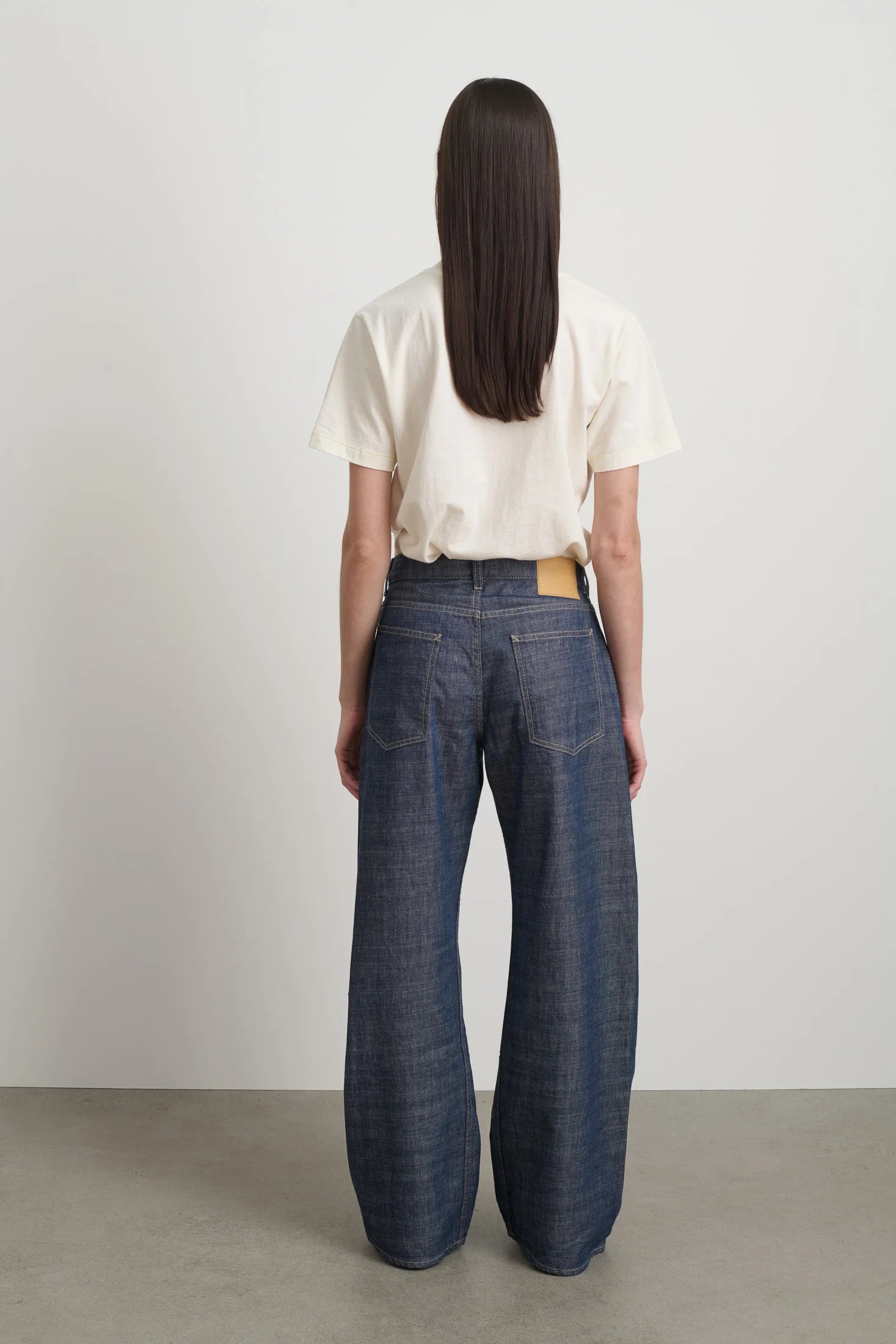 Person wearing a white shirt and blue jeans standing against a plain background