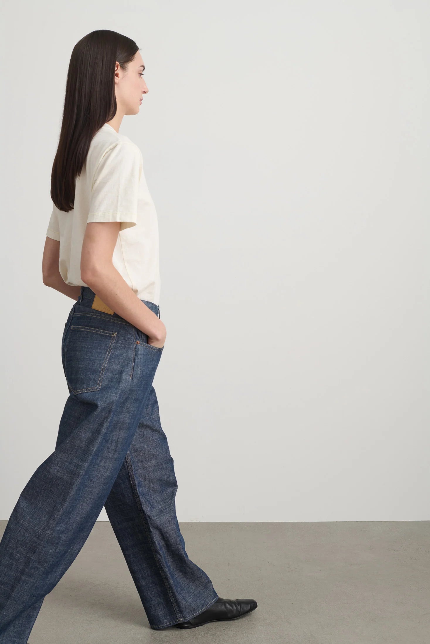 Woman wearing a white shirt and blue jeans walking on a plain background