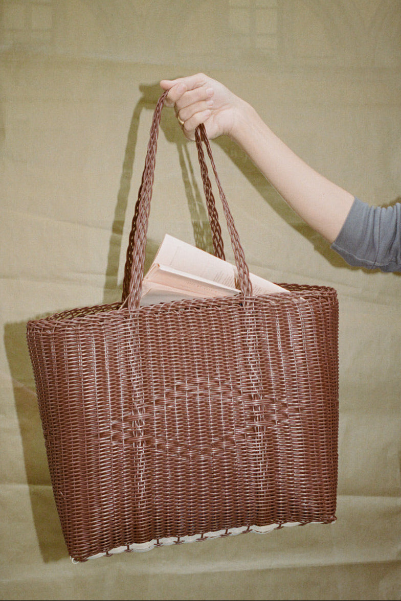 Hand holding a woven brown bag with a neutral background