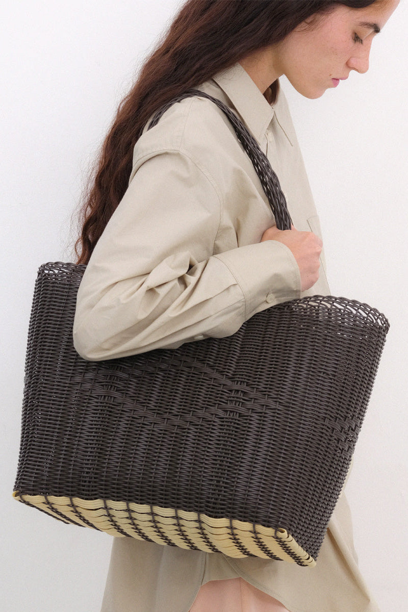 Woman holding a woven brown tote bag with a beige bottom against a white background