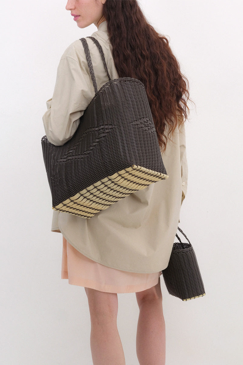 Person wearing a beige shirt, carrying a brown woven tote bag on a white background
