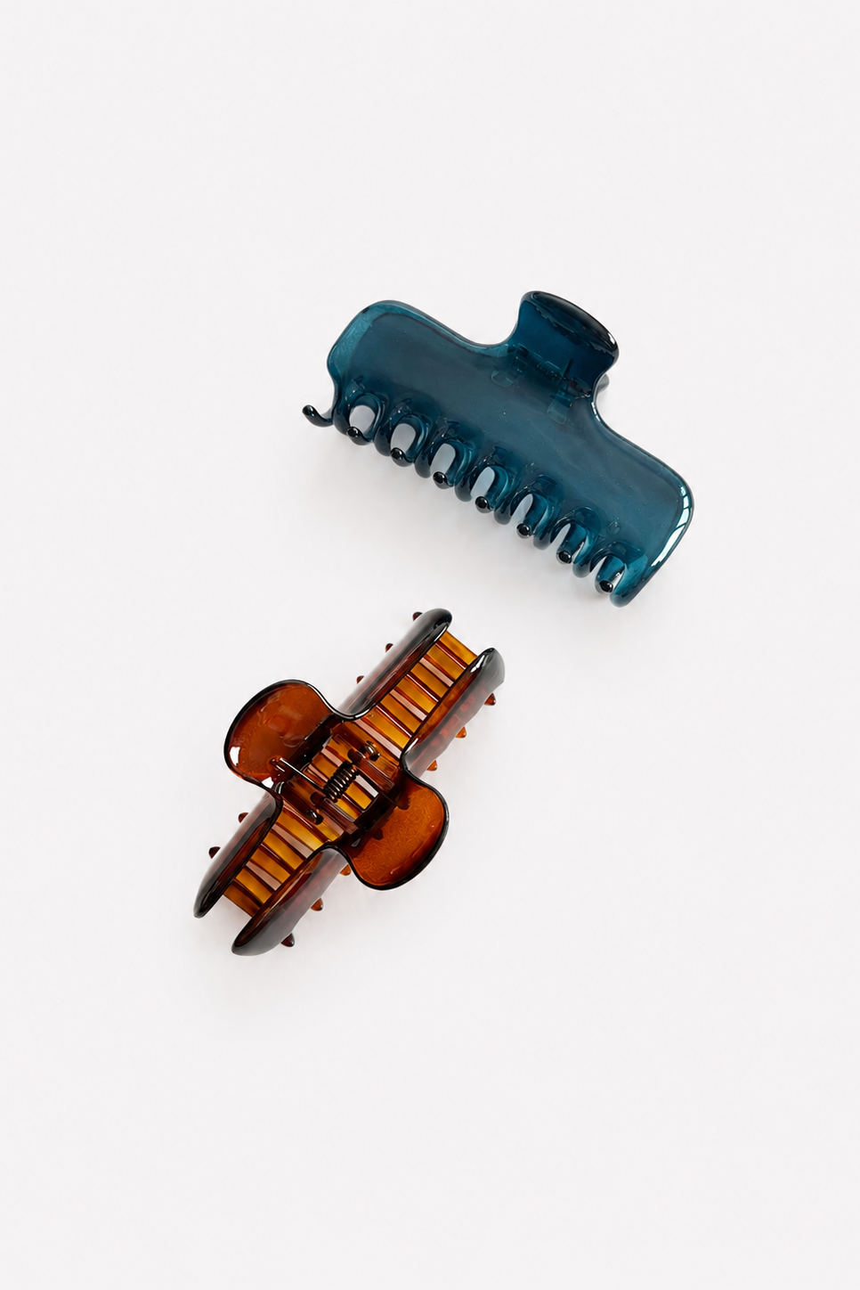 Two translucent hair claw clips on a light gray background, one in dark teal-blue and one in amber-brown with black accents.