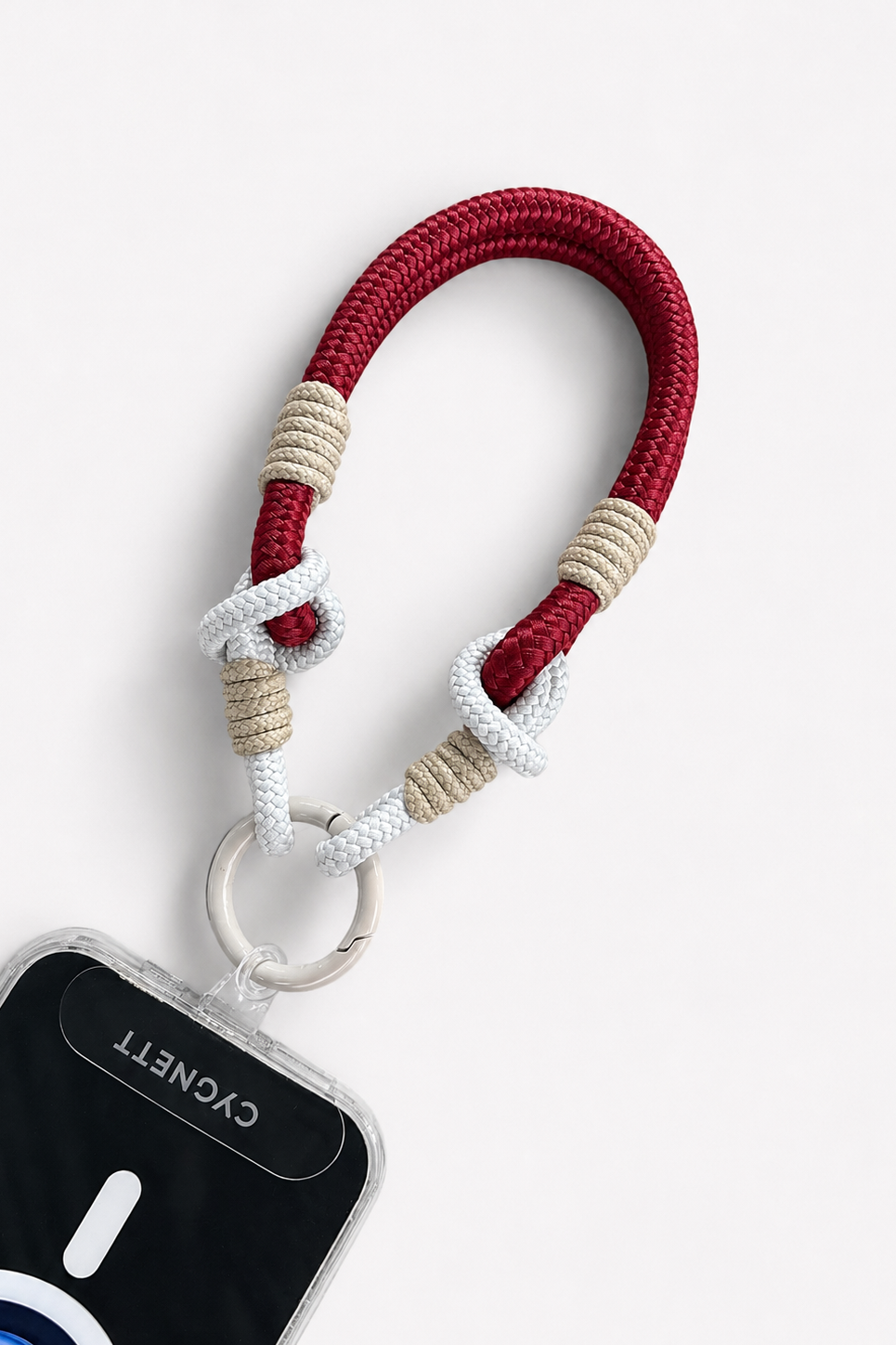 Red, beige, and white braided keychain attached to a phone case on a light gray background