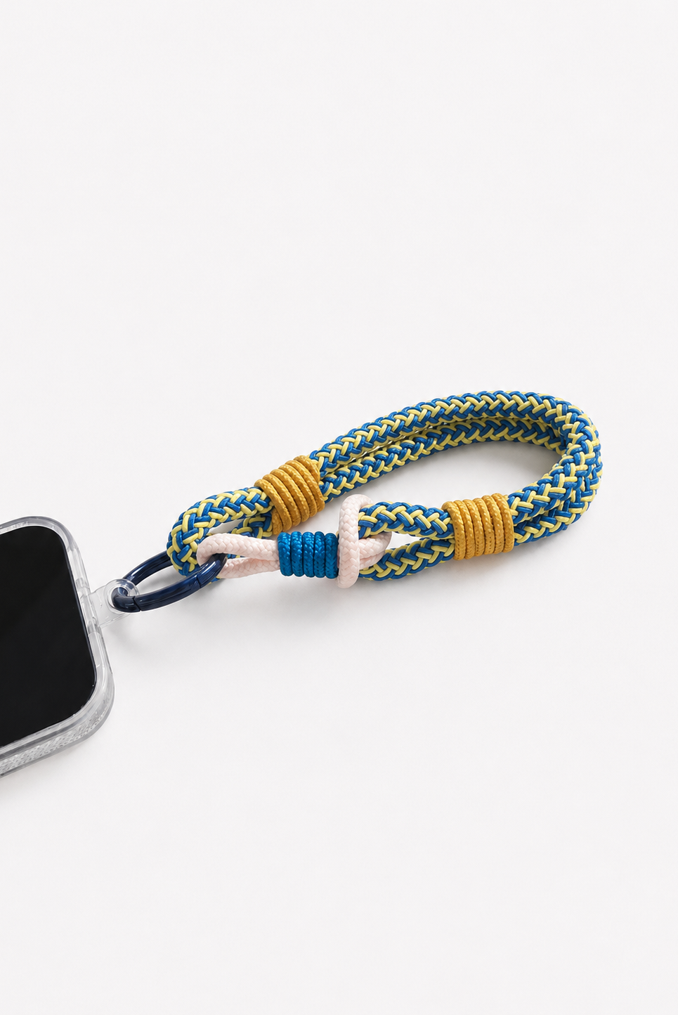 A braided phone strap keychain in blue and yellow, attached to a black carabiner clip. A portion of a smartphone is visible on the left side, set against a clean white background - East Coast General