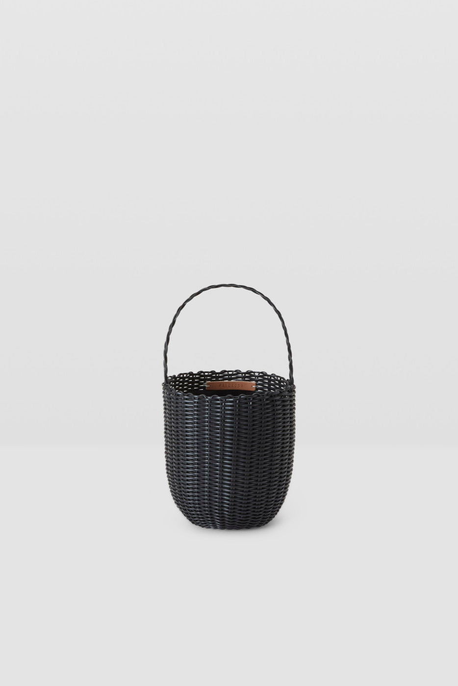 Black woven basket with handle on a light gray background