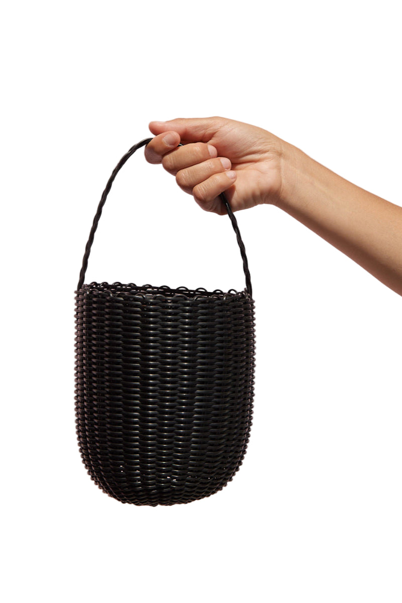 Hand holding a black woven basket against a pink background