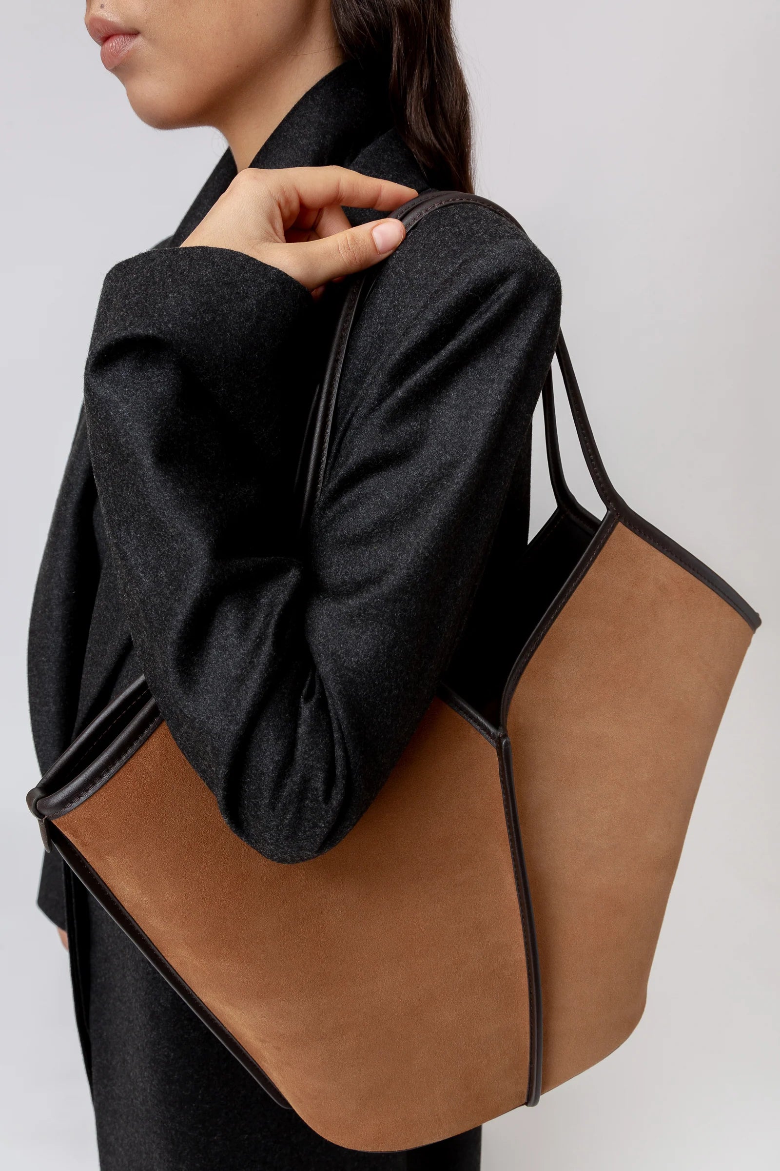 Person holding a brown and black tote bag against a plain background