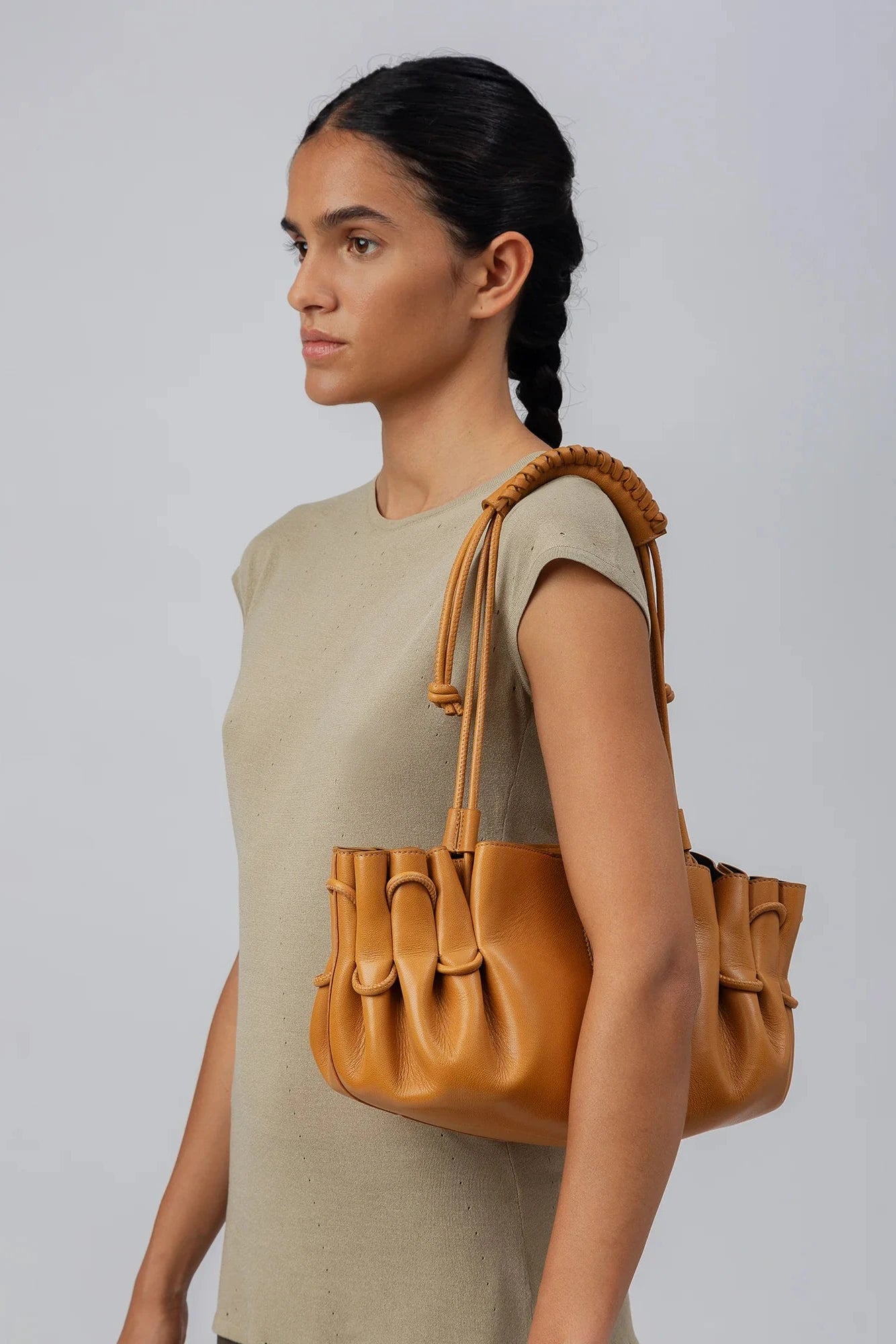 Woman holding a tan leather handbag against a plain background