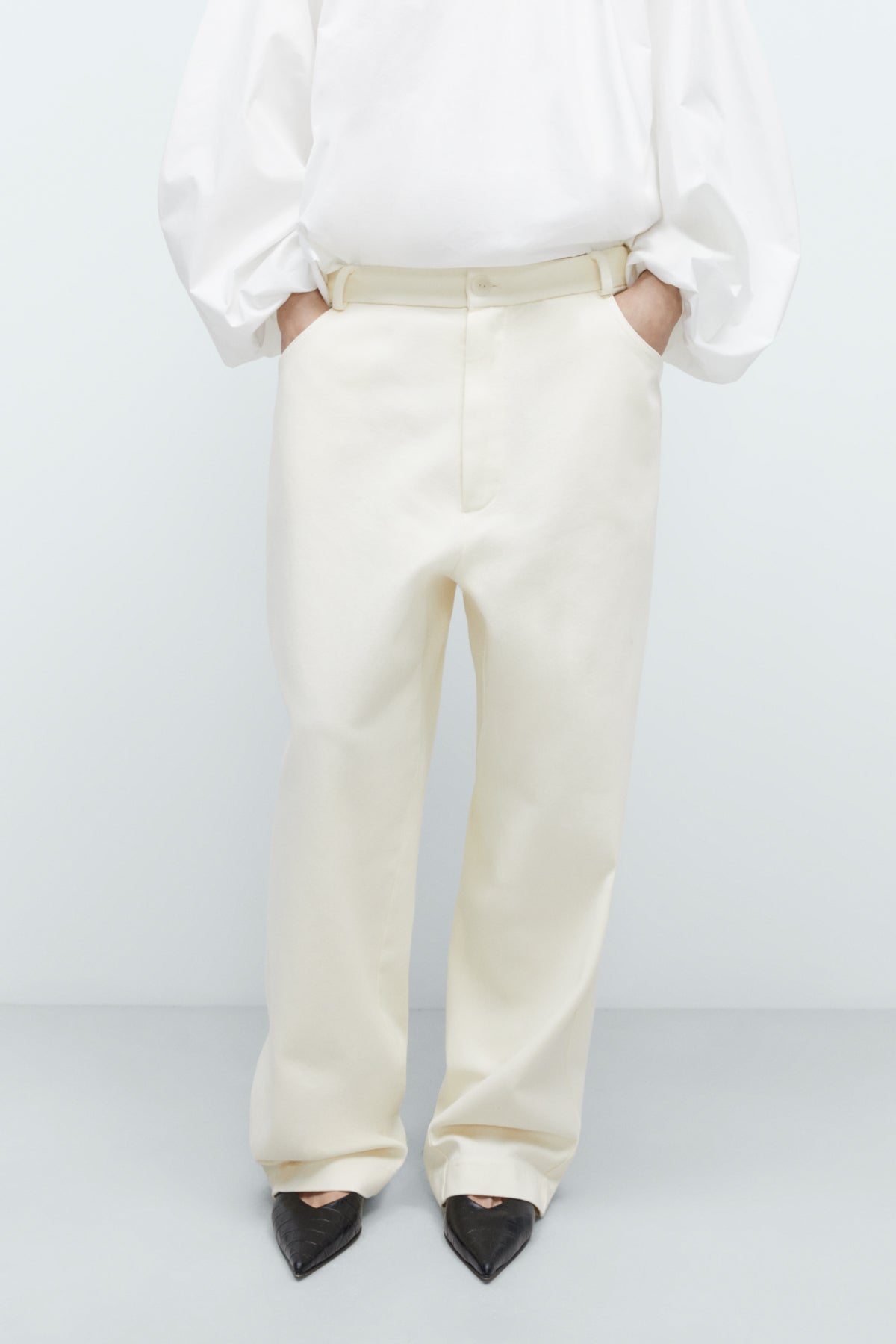 Person wearing a white blouse and cream-colored pants on a light gray background